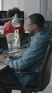 Modern bilişim ofisinde çalışırken Afrikalı Amerikalı erkek yazılım mühendisinin bilgisayarda html program kodunu yazışının dikey yan görüntüsü.