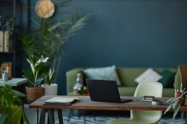 Ahşap masadaki dizüstü bilgisayarla modern ofis içi arkaplan görüntüsü ve yeşil canlı bitkilerle donatılmış duvar boşluğu kopyalıyor.