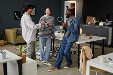 Ofiste kahve molası sırasında sohbet eden ve elinde fotokopi çekilen gülümseyen gençlerin tam boy portresi.