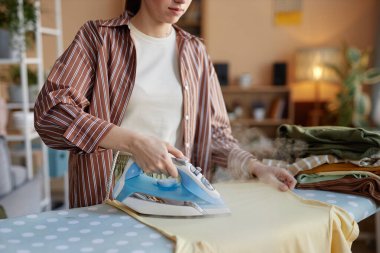 Ütü masasında giysileri ütüleyen ve çamaşır gününde ev işleriyle ilgilenen bir kadın.