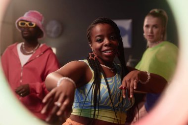 Siyahi genç bir kadının halka ışığından kameraya baktığı sosyal medya için video kaydı yapan dans grubunun portresi