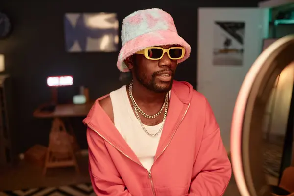 stock image Waist up portrait of trendy Black young man wearing pink outfit and recording videos for social media with ring light