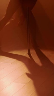 Dikey eğim, akrobatik genç erkek ve kadın direğinin karanlık siluetleri turuncu projektör ışığı altında dans ediyor.