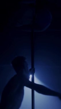 Karanlık odada neon mavi projektör ışığı altında zarif bir performans sergilerken direkte asılı duran ve dönen iki profesyonel direk dansçısının dikey yavaşlaması