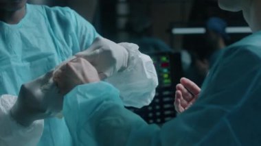 Afrika kökenli Amerikalı kadın asistanın ameliyat odasına hazırlanırken tek kullanımlık mavi cübbeli profesyonel erkek cerrahın eldiven giymesine yardım ederken görüntüsü.