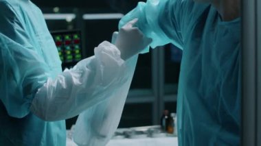 Cerrahın modern hastanedeki ameliyata başlamadan önce steril kol giysisi giymesine yardımcı olan ameliyat asistanı.