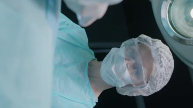 Çalışan yetişkin bir kadın doktorun ameliyat odasında ameliyat yaparken asistanının elindeki metal tepsiden aletleri aldığı dikey bir fotoğraf.