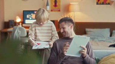 9 yaşındaki beyaz çocuk ve babasının boş zamanlarında birlikte çizim yaparken kanepede sohbet ederken orta boy bir fotoğraf.