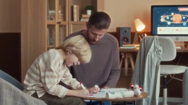 Modern apartman dairesinde babasıyla konuşan ve çizim yapan beyaz bir çocukla orta boy bir fotoğraf.