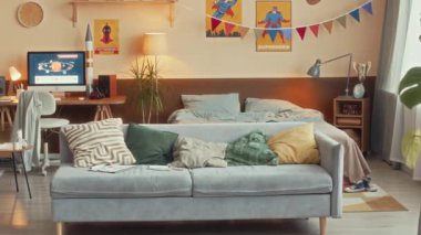 Çocukların yatak odasının içinde yumuşak gri kanepe, masaüstü bilgisayarı ve bej renkli süper kahraman posterleri olan insanlar yok.