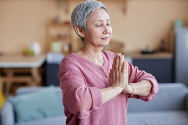 Evde yoga yapmaktan ve meditasyon yapmaktan hoşlanan mutlu son sınıf kadınının belden yukarı portresi.