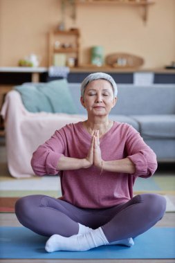 Nilüfer pozisyonunda oturup yoga yapmaktan zevk alan yaşlı bir kadının dikey portresi.