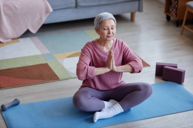 Yoga pratiği sırasında evde meditasyon yaparken gözlerini kapayan sakin yaşlı kadına yüksek açılı bir bakış açısı.