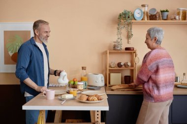 Mutlu yaşlı çiftin sabah rutininin tadını çıkarırken ve birlikte kahvaltı yaparken yan görünüm portresi