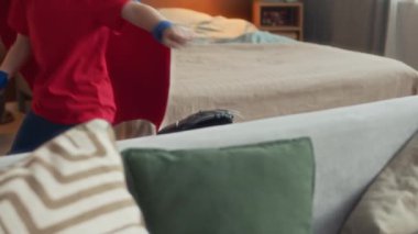 Maskeli ve pelerinli, kırmızı ve mavi takım elbiseli, şakacı, beyaz çocuk evde eğlenirken kanepede zıplayıp duruyor.