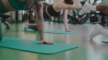 Pozitif genç Kafkas dövmeli kadın jimnastik koçu paspasın üzerinde denge masası pozu veriyor.