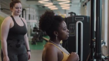 Orta boy Afro-Amerikan bir kadının spor salonunda spor salonunda, teknik açıklamasıyla kelebek pres makinesi üzerinde egzersiz yaparken.