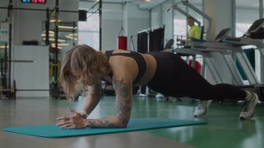 Beden eğitiminde yoga minderinin üzerinde kalas pozisyonunda dururken vücut egzersizleri yapan aktif beyaz kadın.