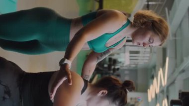 Spor salonunda kadın fitness eğitmeniyle çalışırken kelebek pres makinesi üzerinde egzersiz yapan kıvrımlı genç beyaz kadının dikey orta pozu.