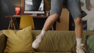 Pembe gözlüklü ve apartmandaki kanepede dans eden modaya uygun, çift ırklı kız.