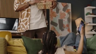 Çift ırklı adamın elinde hediye kutusuyla kanepede uzanıp akıllı telefondan kısa videolar izlediği orta boy bir fotoğraf. Saç kurutma makinesini kutudan çıkaran kız mutlu oluyor.