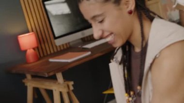 Çift cinsiyetli yavaş adam, gülen kız arkadaşını salona yuvarlıyor sonra öpüşüyor, modern dairede birlikte eğleniyor.