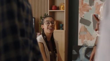 Havalı gözlüklü, havalı, çift cinsiyetli bir adamın dairesindeki aynanın önünde oturan sevgilisine mavi kareli gömlek giydirdiği orta boy bir fotoğraf.