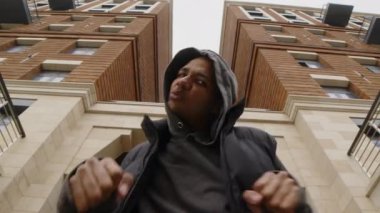 Arka planda modern apartman binası ile hip hop dansı yaparken kameraya bakan iki yüzlü adamın düşük açılı bıçak yavaşlığı.