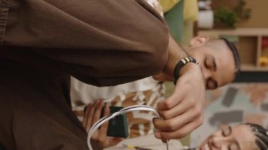 Genç Z jenerasyonunun dikey orta pozu. Çift ırklı çift koltukta rahatça oturup akıllı telefona bakıyor ve sohbet ediyorlar.