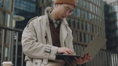 Şehirdeki açık havada laptopta çalışan ya da ders çalışan Asyalı genç bir erkeğin orta boy fotoğrafı.