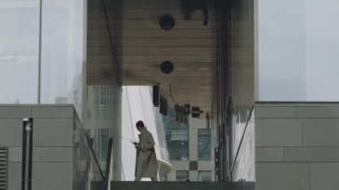 Geniş açılı, şık ve şık giyinmiş genç adam şehir merkezinde telefon görüşmeleri yaparken iki cam duvarda dolanıp duruyor.