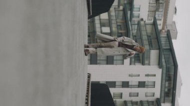 Asyalı genç bir adamın bir fincan kahveyle kaldırımda yürüdüğünü gösteren dikey ve yavaş bir çekim.