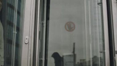 Çağdaş ofis binasından dönen cam kapılardan içeri giren Asyalı genç işadamının orta derece yavaşlığı.