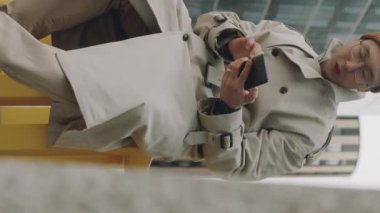 Asyalı adamın akıllı telefondan numara çevirdiği ve gündüz vakti bankta otururken arama yaptığı dikey düşük açılı çekim.