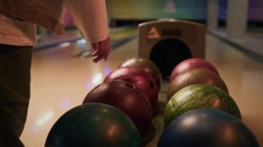 Tanımlanamayan bovling oyuncusunun arka planda 10 lobutu bulanık bir şekilde bovling topunu kulvardan seçmesi.