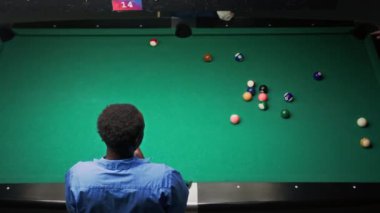 Barda yeşil masada bilardo oynayan Afrikalı bir adamın yüksek açılı yavaş çekimi.
