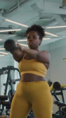 Spor salonunda kettlebell egzersizi yapan renkli giysili iki genç kadının dikey orta pozu.