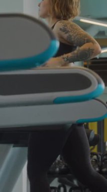 Kafkas formalı genç bir kadının spor salonunda koşu bandında koşarken dikey yan görüntüsü.