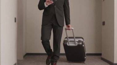 İyi giyimli genç bir Orta Doğulu erkek girişimcinin bavuluyla otel odasına girerken ve büyük boy yatağa uzanmış mesajlaşırken ve akıllı telefonlarda gezinirken görüntüsü kesildi.