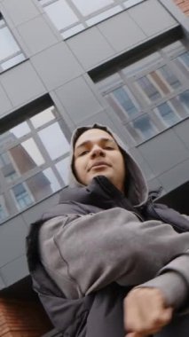 Kırmızı tuğlalı apartmana karşı kaldırımda dikilirken gri kapüşonlu adamın kameraya poz verdiği kendine güvenen hippinin el kamerası görüntüsü.