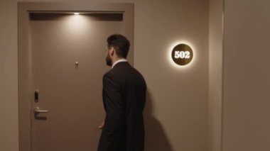 Formalite icabı giyinmiş, bavullu, otel odasının kapısını açan ve içeri giren kendine güvenen iş adamının orta görüş açısı.