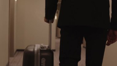 Uzun otel koridoru boyunca odasına doğru yürürken, takım elbiseli, tanınmamış bir işadamının görüntüsü.