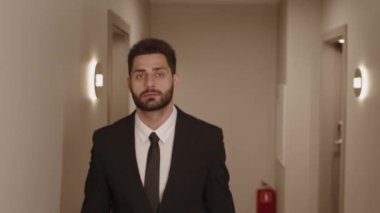İyi giyimli Orta Doğulu ciddi bir iş adamının lüks oteldeki koridorda yürürken orta açıdan çekilmiş fotoğrafı.