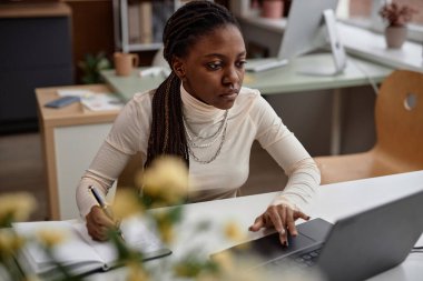 Ortak çalışma alanı, ofis ya da sınıfta laptopta çalışan odaklanmış genç Afrikalı Amerikalı bir kadının orta boy fotoğrafı. Öğrenci sınavlara hazırlanıyor, notlar alıyor, kendi kendine çalışma kavramı, kopyalama alanı