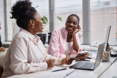 Two African American female colleagues friendly chatting looking at each other. Pausing from work in office setup, focus on one woman, copy space clipart