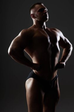 Önden yayılan güçlü sporcunun dikey arka plan portresi karanlık arkaplanda göğüs kaslarını genişletiyor.