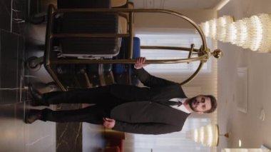 Lüks otel lobisinde bavul vagonunda duran üniformalı orta doğulu bellboyun dikey portresi.