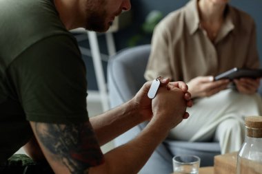 Duygusal terapi seansında, kederle ve travma sonrası stres bozukluklarıyla uğraşırken, elinde künyeli künyeyle tanınamaz hale gelen askerlerin yakın çekim görüntüleri.