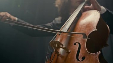 Erkek klasik müzisyenin solo konser sırasında siyah arka planda tiyatro sahnesinde çello çalması.