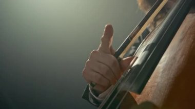 Beyaz erkek klasik müzik sanatçısı pembe saçlı siyah arka planda tutkuyla çello çalıyor.